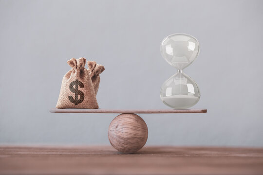 Financial concept : Write sand clock or hourglass symbol and dollar bagson a balance scale in equal position.Time value of money, asset growth over time, investment in long-term equity for more money 