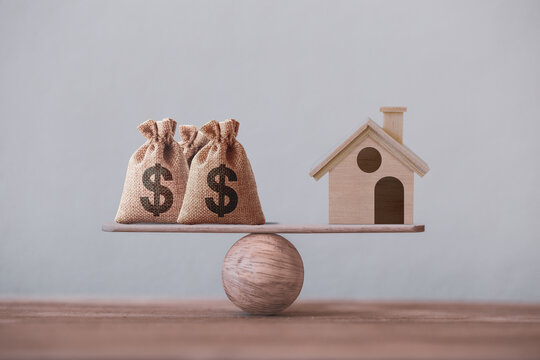 US dollar hessian bags with house paper model on a wood balance scale. Home loan, reverse mortgage concept, Depicts a homeowner or a borrower turns properties into cash
