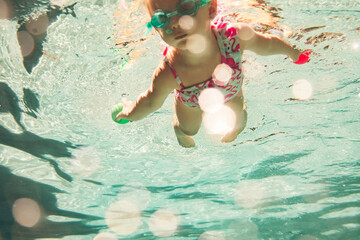 little girl in swimming swimsuit and glasses swimming underwater in the pool 