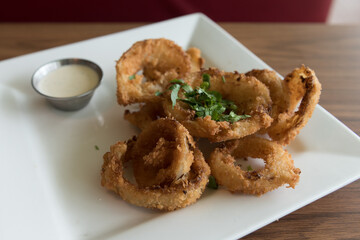 Kuala Lumpur, Federal Territory / Malaysia - February 24, 2017: A platter of deep fried onion ring with cuts of cilantro on top served in white square shape plate with side dip.
