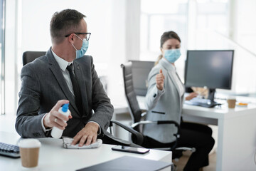 Handsome businessman disinfecting desk in the office.	