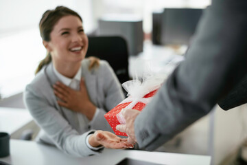 Young businessman giving his colleague present in office. Young man suprise beautiful businesswoman...