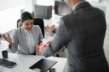 Young businessman giving his colleague present in office. Young man suprise beautiful businesswoman in office.	
