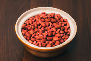 A bowl of peanuts with husks is isolated on a wooden background. Nuts for making peanut butter. Vegan food