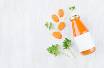 Fresh orange carrot juice in glass bottle with blank label, ingredients and green leaves on white wood board, mock up for design, advertising, branding identity product.