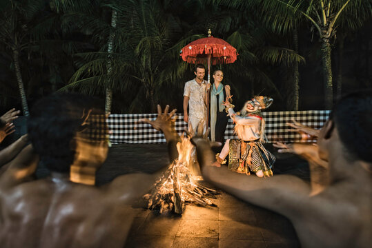 Asia, Indonesia, Bali, young Caucasian couple, wearing smart casual clothing, enjoying a traditional Balinese Kecak dance performed around a fire, at night, with Hanuman the monkey god.