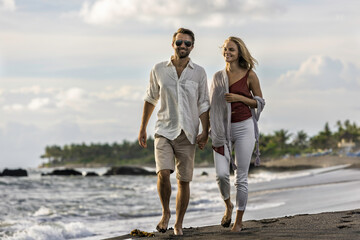 Asia, Indonesia, Bali, young Caucasian couple walking along a empty, secluded beach in Bali, holding hands, wearing smart casual clothing, while on holiday.