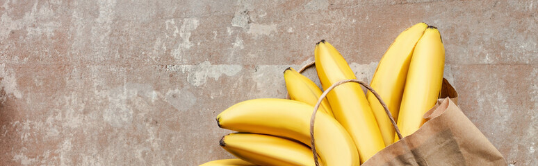 top view of paper bag with bananas on beige weathered surface, panoramic crop