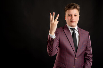 Law student with blond hair dressed in burgundy jacket, white shirt and black tie counting three with his finger