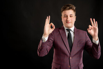Law student with blond hair dressed in burgundy jacket, white shirt and black tie showing double OK sign