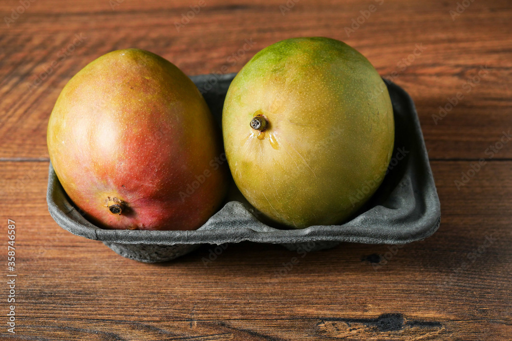 Wall mural two fresh ripen mango in a grey container on a wooden table surface, fresh fruit industry concept.