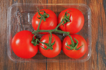 Fresh and ripe tomatoes on a vine in a plastic container on a wooden table surface, Fresh produce product.