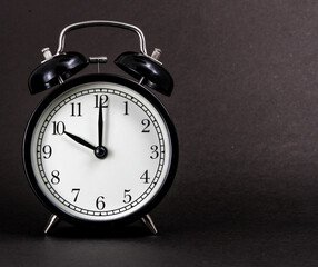 An old alarm clock showing 10 o'clock on a black background