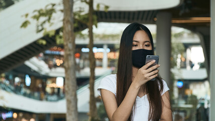 Woman wearing a mask and using a smartphone for business, social media, working and waiting for someone in the public.