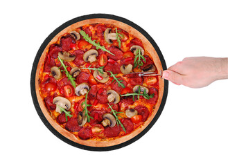 The chef cuts the pizza hot with a pizza cutter. Tasty pizza with salami, arugula, cherry tomatoes, mushrooms and texas spice mix, on a slate black platter, isolated on white background