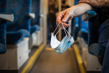 Woman sitting in train alone and holding face mask in her hand. New normal during travel in...