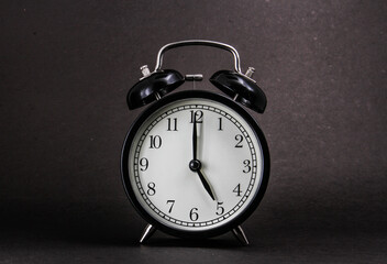 An old alarm clock showing 5 o'clock on a black background