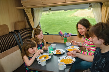 Family eating together in RV interior, parents and kids travel in motorhome (camper, caravan) on...