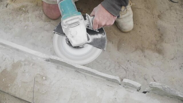 Man kneeling using power tool on construction site, cutting stone paving