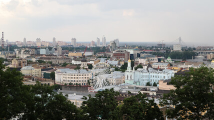 Fototapeta premium The view from the height of the Podolsky district of the city of Kiev, the old square with a Ferris wheel and a bell tower with a gilded dome. Beautiful cityscape in the summer.