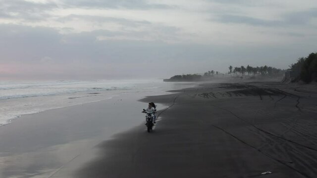 Drone aerial of couple on motorcyle at blacks sand pasut beach in Bali Indonesia