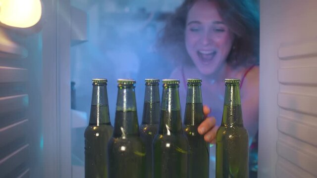Young woman open fridge door and take beer bottle