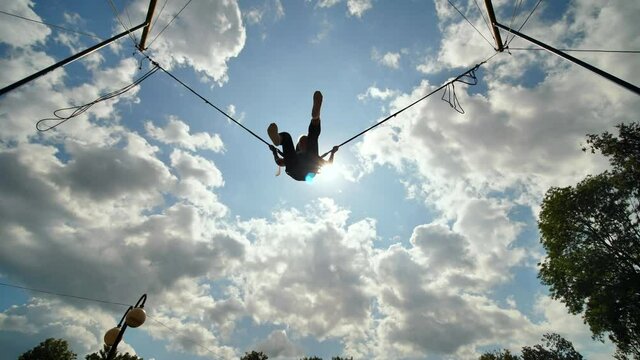 Teenage girl silhouette jumping on the trampoline bungee jumping. Slow motion video.