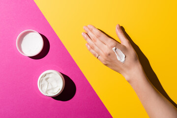 partial view of female hand near container with hand cream on pink and yellow