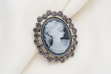 Cameo brooch, which is a side portrait of a woman, with small crystals around the edges on a white background. - obrazy, fototapety, plakaty