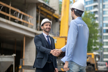 Building supervisor and foreman greeting, shaking hands with each other on building site