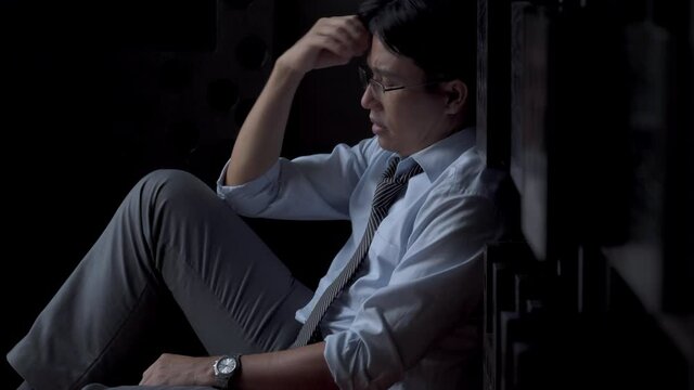 4K Stressed Asian businessman entrepreneur sitting on the floor thinking of business and debt problem. Depressed unemployed man worried and tired of work. Mental health and economic problem concept