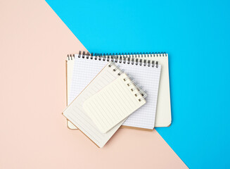 stack of spiral open notebooks with blank white sheets on a blue background