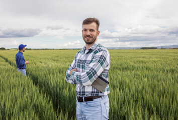 Portrait of farmer standing in green wheat field with his colleague in background.