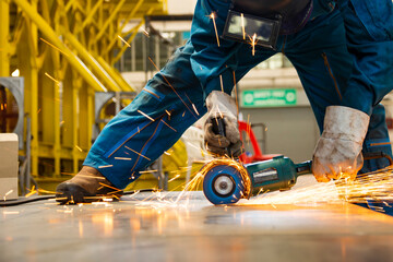 worker in blue uniform cutting metal sheets with electric grinder in the workshop. Mechanic wear...