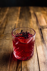 A hibiscus cocktail with an ice cube in a rocks glass on wooden table