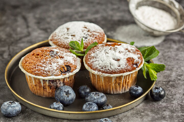 Several fragrant muffins with blueberries are on the table, next to blueberries and mint.