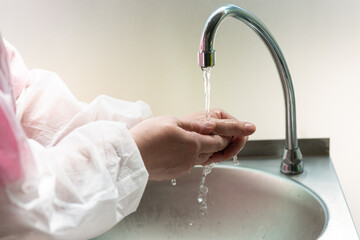 a woman in a white coronavirus protective suit is washing her hands on a tap with falling water. hospital. doctor, nurse, physiotherapist, osteopath.