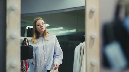 Attractive woman trying on handbags in front of a mirror in a boutique