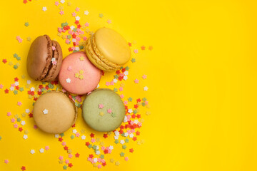 Macarons sabrosos de diferentes sabores sobre un fondo amarillo brillante liso y aislado con decoraciones de estrellitas de colores. Vista superior. Copy space