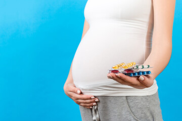 Close up of pregnant woman holding a pile of blisters of pills at colorful background with copy space. Vitamins during pregnancy concept