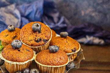 Several fragrant muffins with blueberries are on the table, next to blueberries and mint.