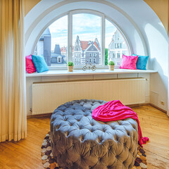 Modern interior of living room in luxury apartment.  Semicircle window. View of old town of Riga. Cozy large pouf and TV.