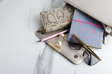 Closeup of woman bag, purse, sunglasses, notebook, pen, bottle of fragrance on the white marble table.Empty space
