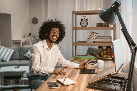 Young student or enterprener engaged in creative work using a graphics tablet and computer. Arabic guy in eyeglasses smiles looking at camera. Work from home concept. Tinted image.