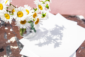 White blank sheet and a bouquet of daisies in a glass jar on a wooden background. Symbol of purity and freshness, skin cosmetics
