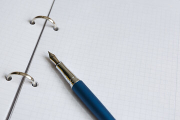 White sheet of notebook or diary in a cage. Open school notebook with rings. Blue metal fountain pen