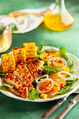  Grilled chicken breasts cooked on a BBQ served with citrus salad and corn on a plate. Close up view. Concept homemade summer dinner