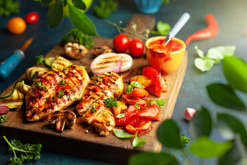 Grilled chicken breasts and different vegetables ad mushroom cooked on a BBQ served on wooden board. Close up view. Concept homemade summer barbeque dinner