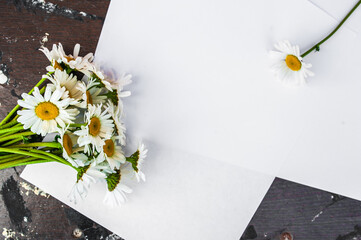 White blank sheet and a bouquet of daisies on a wooden background. The concept of cleanliness, perfume, skin care