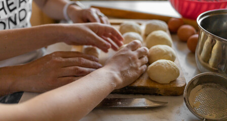 Fototapeta na wymiar Women's and children's hands in the kitchen are prepared from dough. On the cutting board are several balls for the future pizza. High quality photo